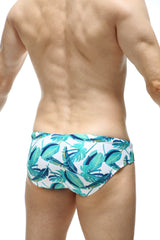 White swim trunks by petitq featuring vibrant teal and dark blue tropical leaf pattern for beachwear