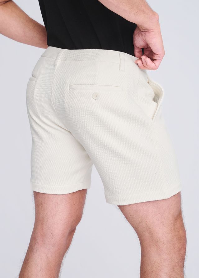 Cream-colored textured stretch knit chino shorts showing the back with a small buttoned pocket and tailored fit