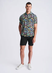 A man wearing a floral lightweight linen tencel short-sleeved shirt with a multicolored pattern on a dark background