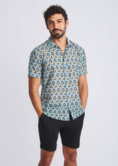 A man wearing a swirls lightweight cotton silk short-sleeved shirt with blue teal and orange geometric pattern