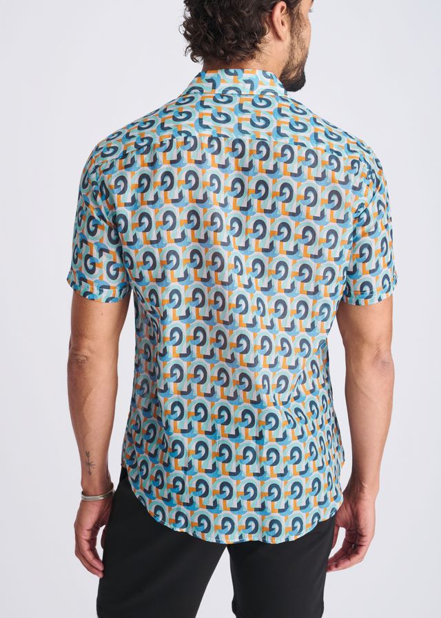 A man wearing a swirls lightweight cotton silk short-sleeved shirt with dark blue and orange geometric patterns on turquoise