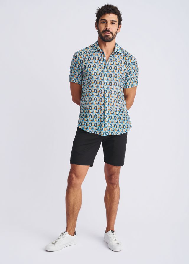 A man wearing a swirls lightweight cotton silk short sleeve shirt with blue green and yellow circular pattern on teal background