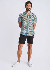 A man wearing a swirls lightweight cotton silk short sleeve shirt with blue green and yellow circular pattern on teal background