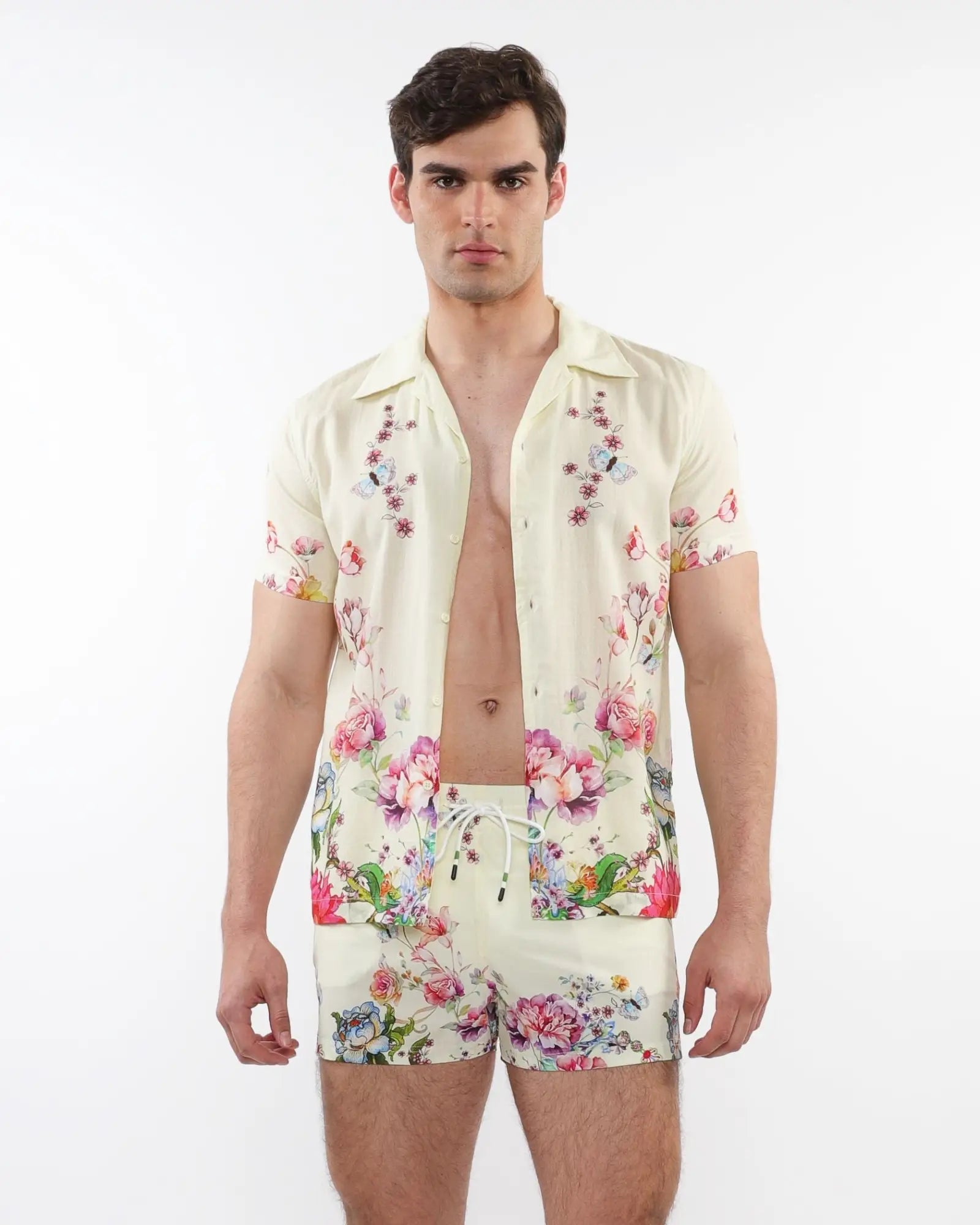 A man wearing a cream printed s s woven modal border shirt and matching shorts with vibrant floral patterns