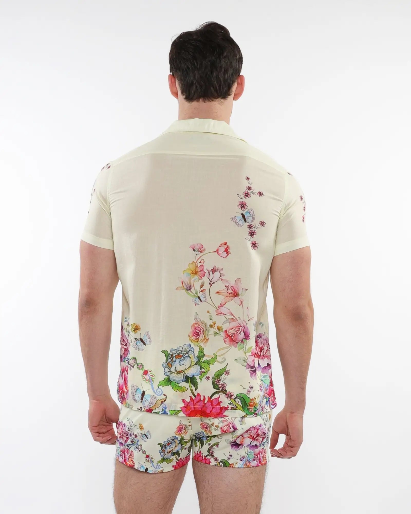 A man wearing a cream short-sleeved printed modal shirt with vibrant floral and butterfly patterns