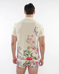 A man wearing a cream short-sleeved printed modal shirt with vibrant floral and butterfly patterns