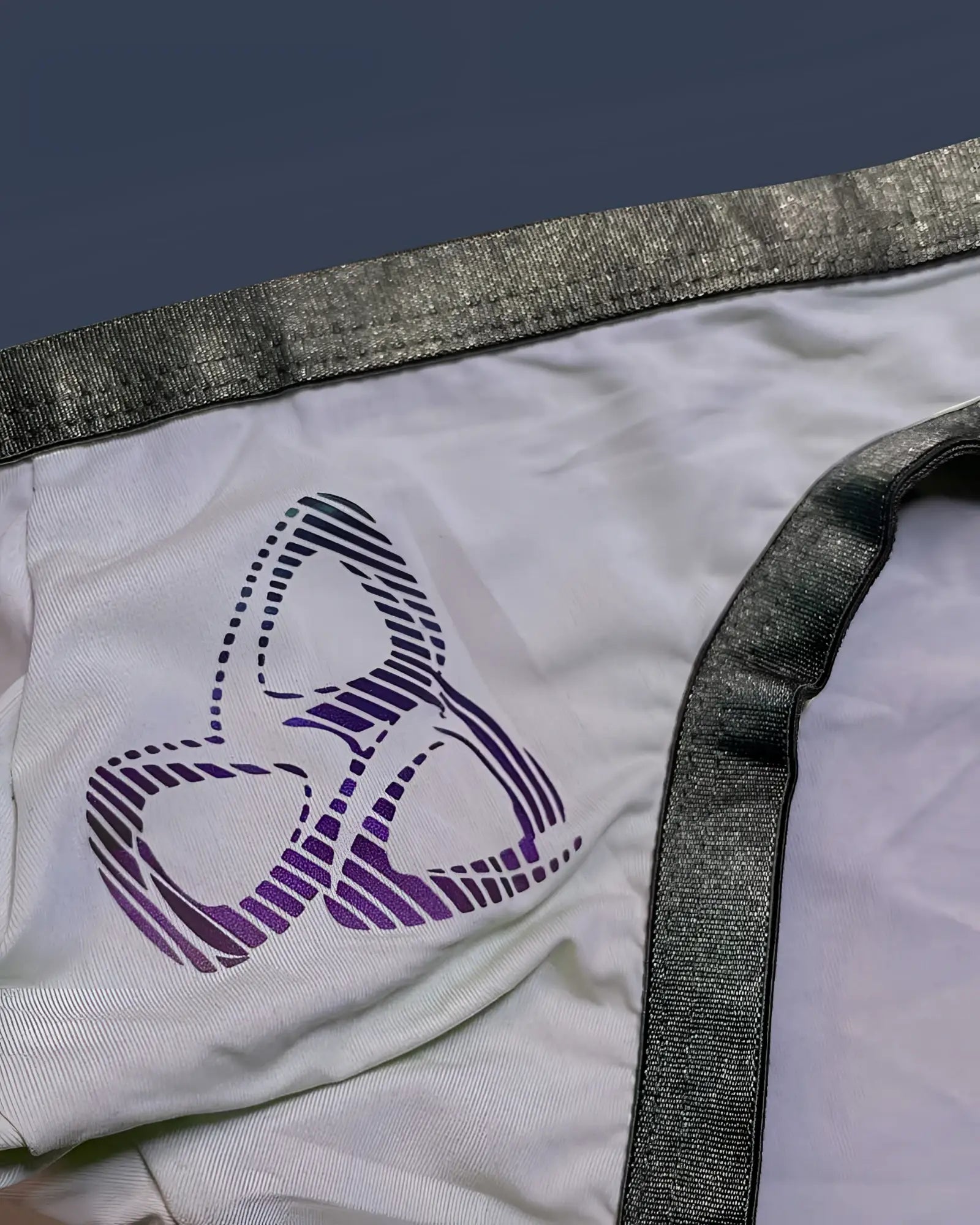 White fabric bikini underwear with purple and black striped abstract logo and shiny gray elastic waistband trim by private structure