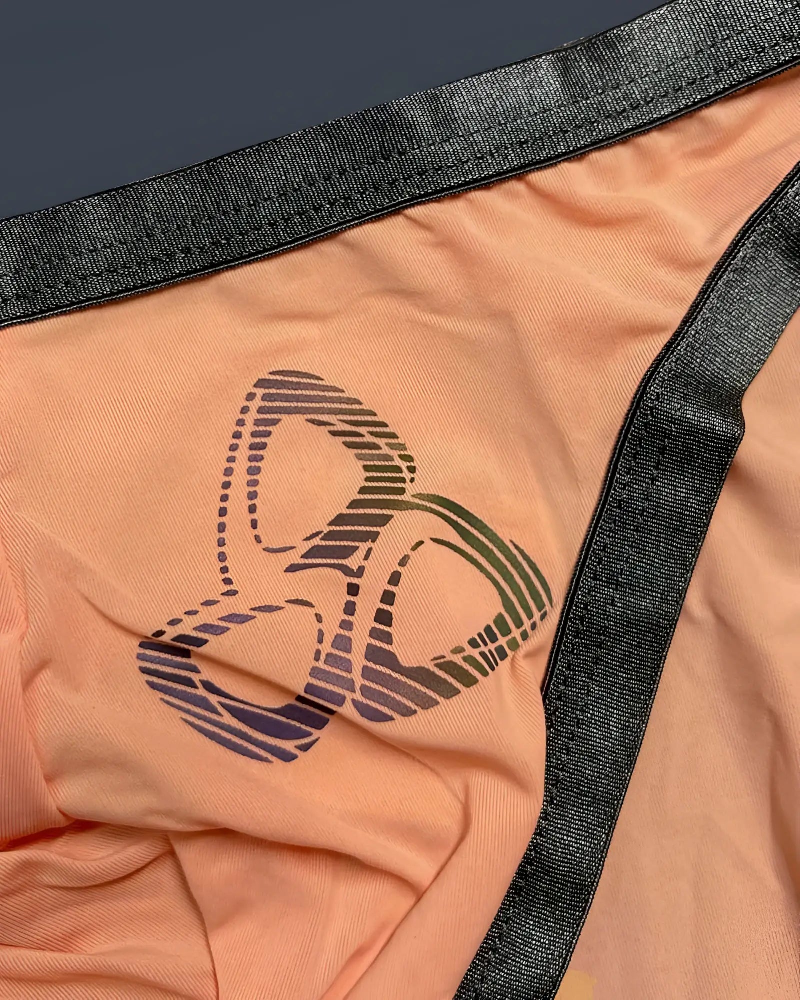 Peach-colored fabric thong with black elastic trim and gradient-striped logo from private structure bare bikini color orange