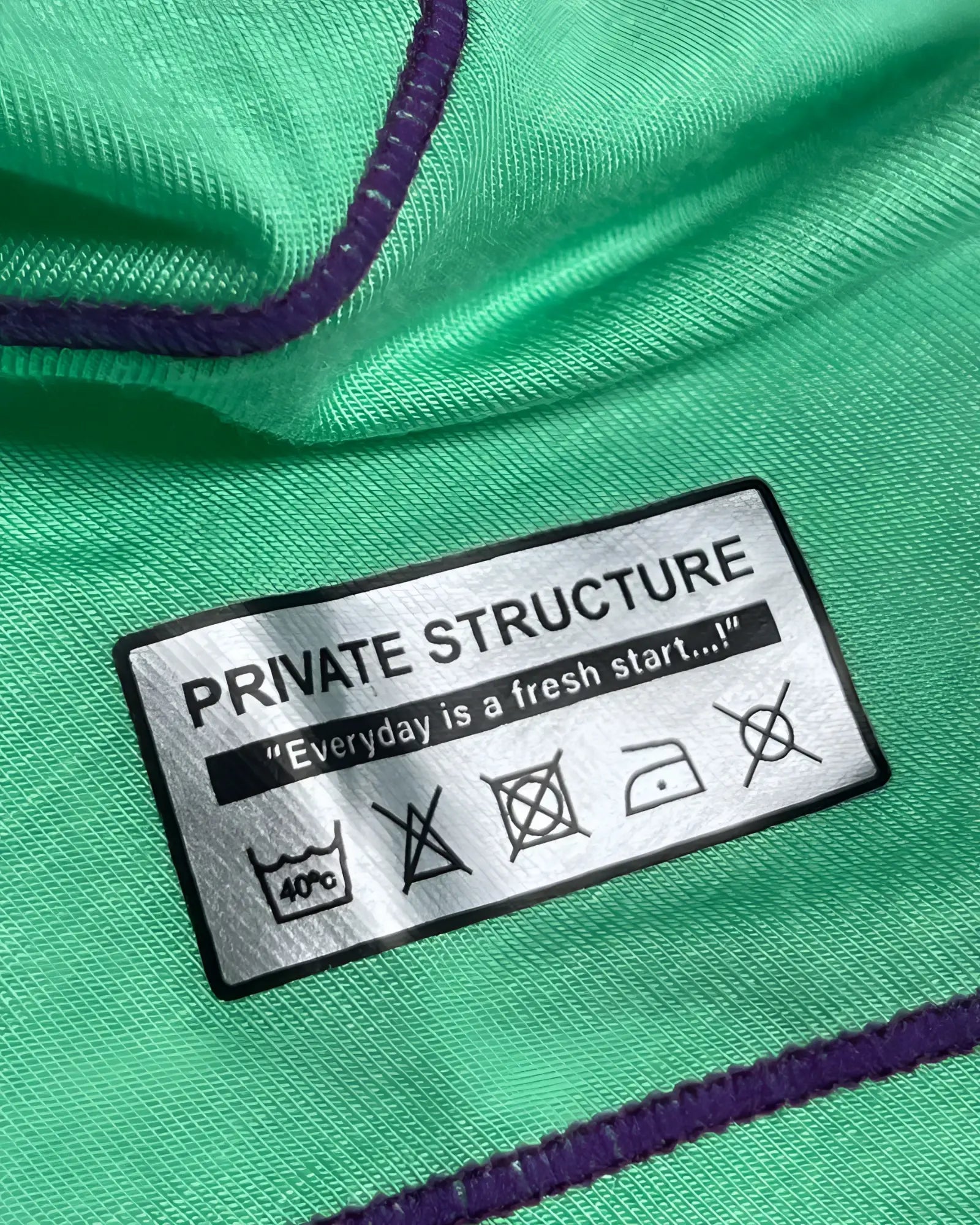 Green fabric with purple stitching and a silver private structure label showing care instructions on the epus4570 hipster