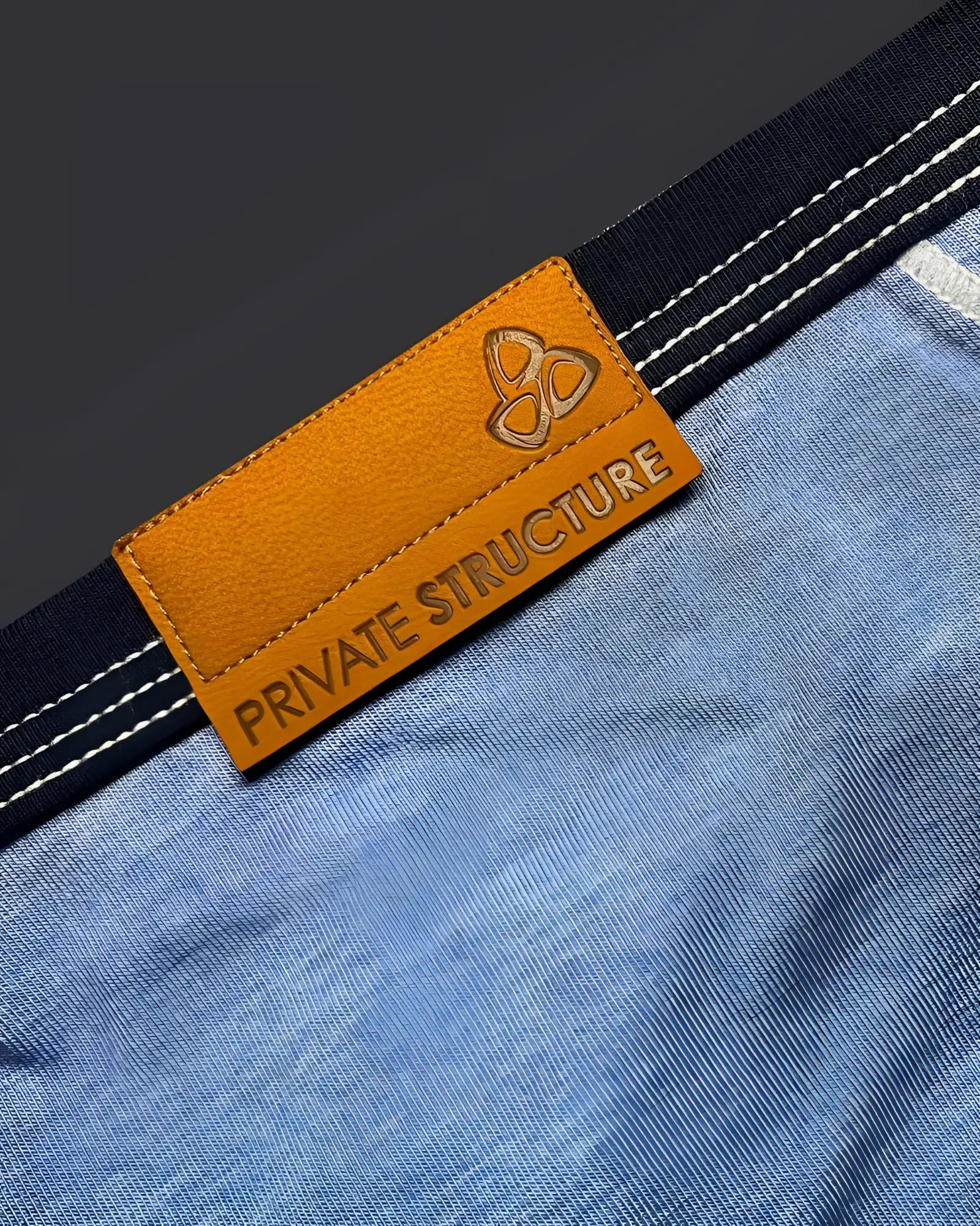 Orange leather brand tag with embossed logo and private structure text on blue denim fabric of barn boy mini brief