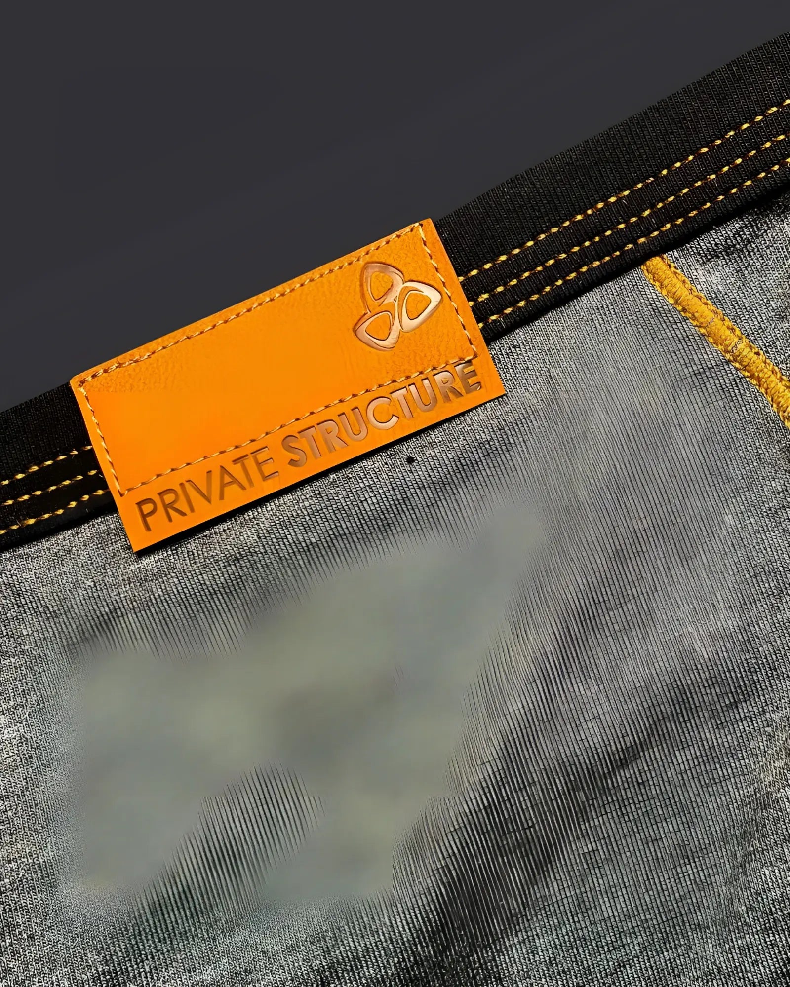 Orange leather brand tag with embossed logo and private structure text stitched on dark gray denim of stone gray low rise mini brief