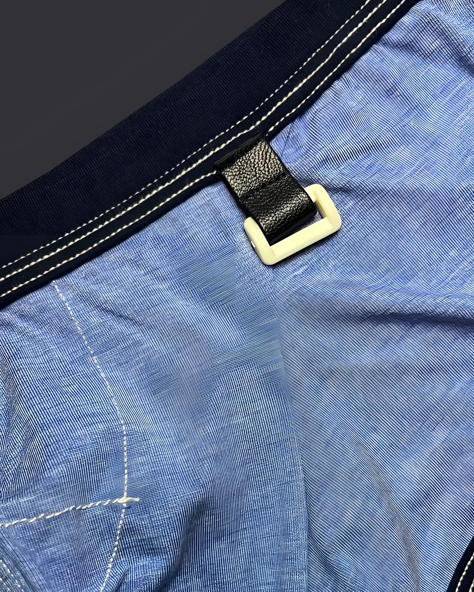 Black leather strap with cream plastic buckle attached to blue denim fabric on private structure barn boy low rise trunk
