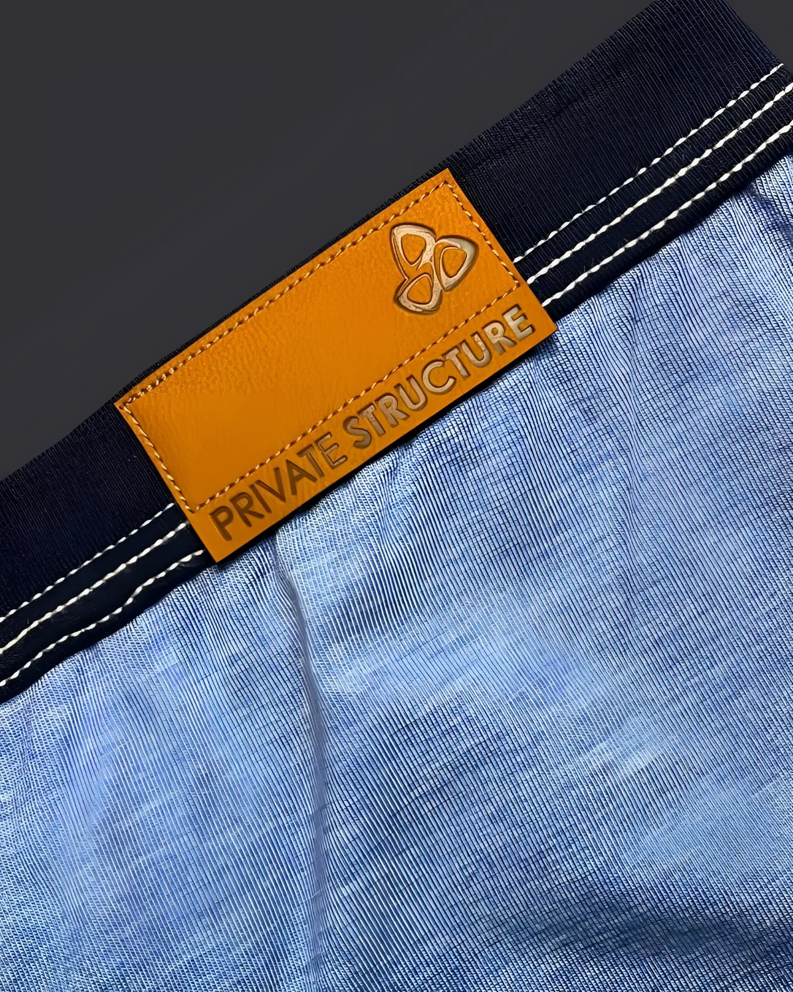 Orange leather brand tag with embossed logo and private structure text sewn on dark blue denim waistband of private structure lcut4359 barn boy low rise trunk