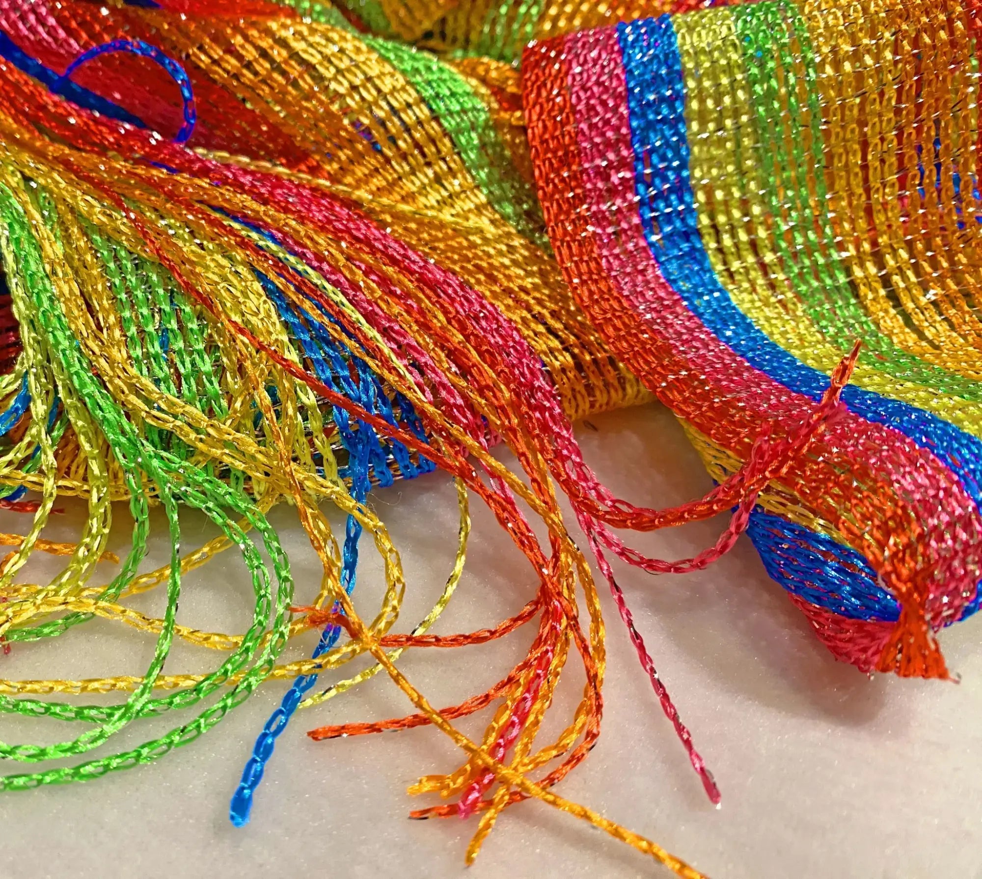 Rainbow glitter poncho featuring rainbow-colored glittery mesh ribbon with woven texture and fringed ends