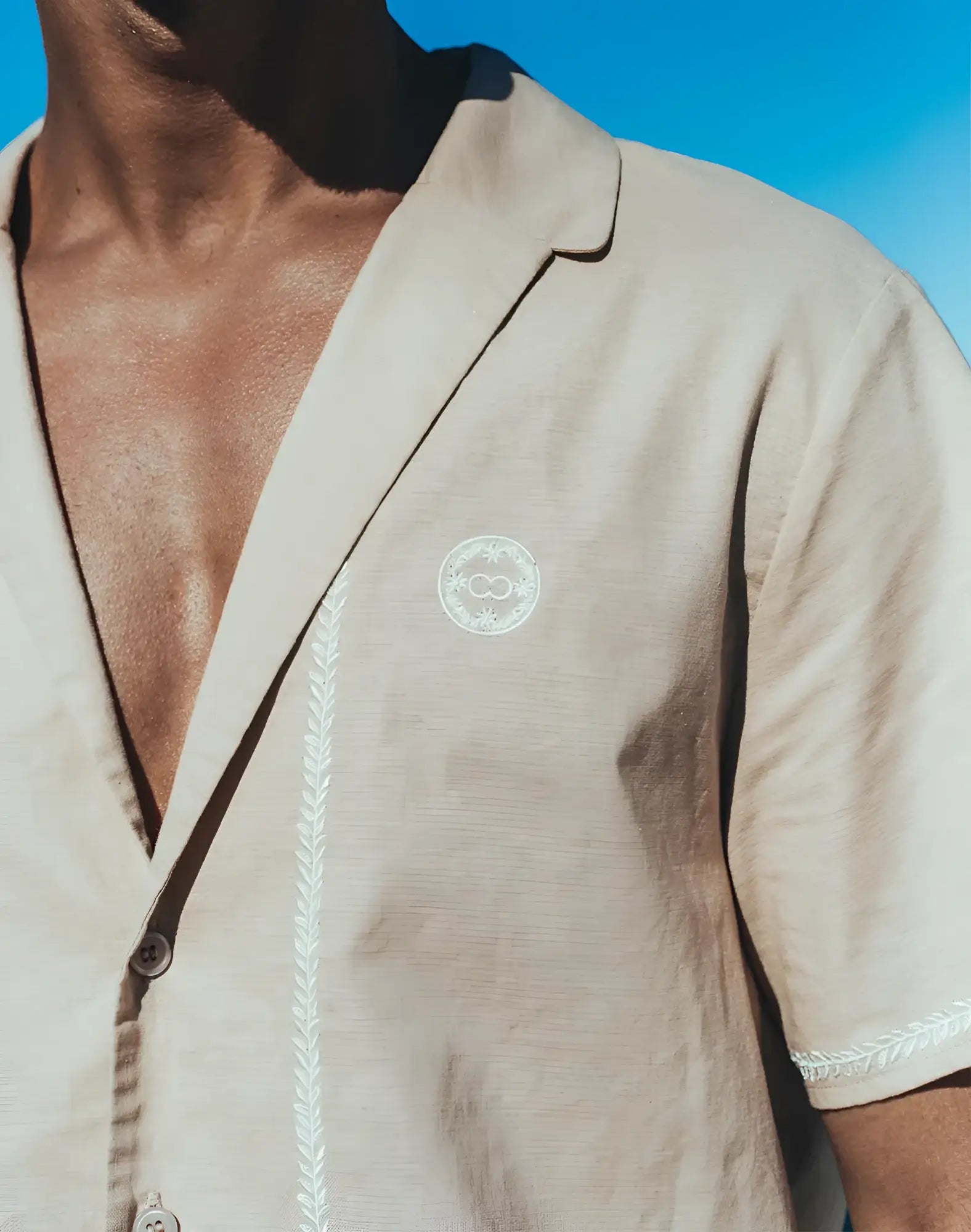 Beige santorini linen shirt with short sleeves white embroidered detailing and circular logo on the chest