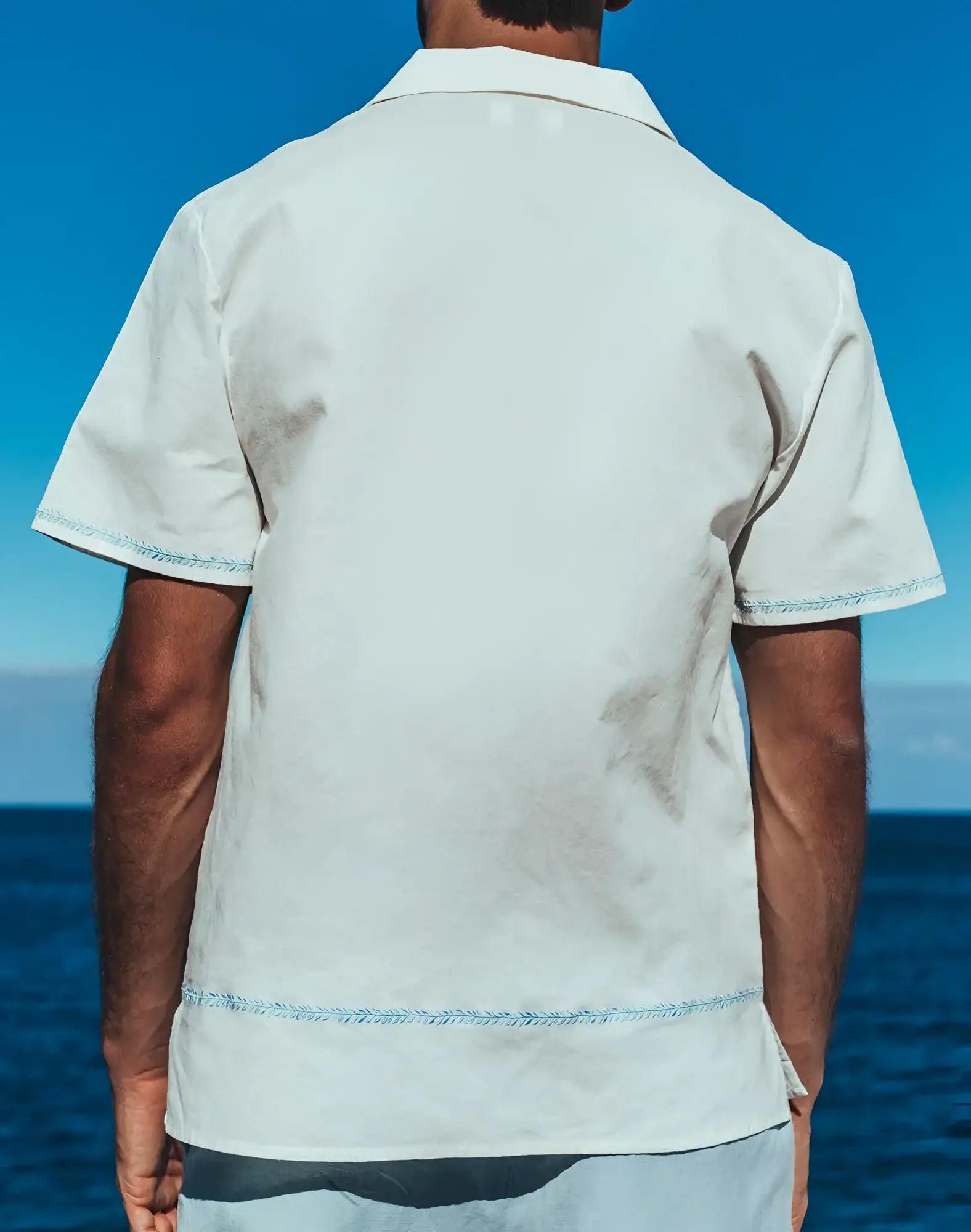 Santorini linen shirt is a crisp white short-sleeved button-up with light blue decorative stitching on hem and cuffs