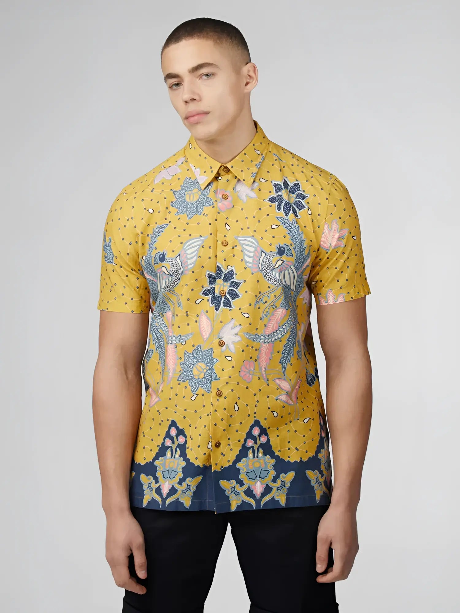 Yellow short-sleeved button-up shirt with intricate blue pink and white floral and bird patterns on dotted background
