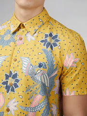 Yellow short-sleeved button-up shirt with intricate blue pink and white floral and bird patterns on textured fabric