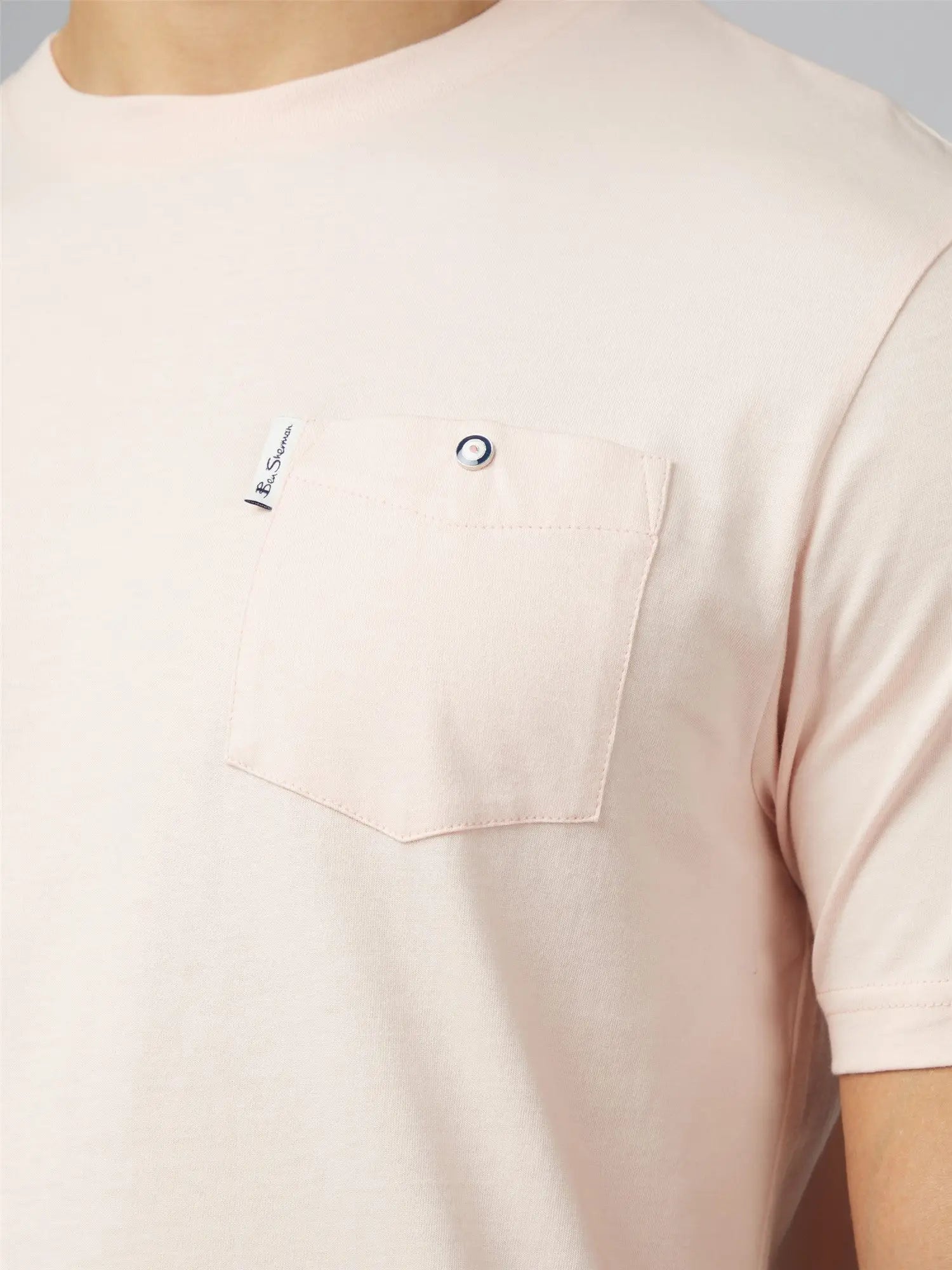 A soft blush pink signature t shirt with chest pocket featuring silver button closure and branded tag on upper left corner