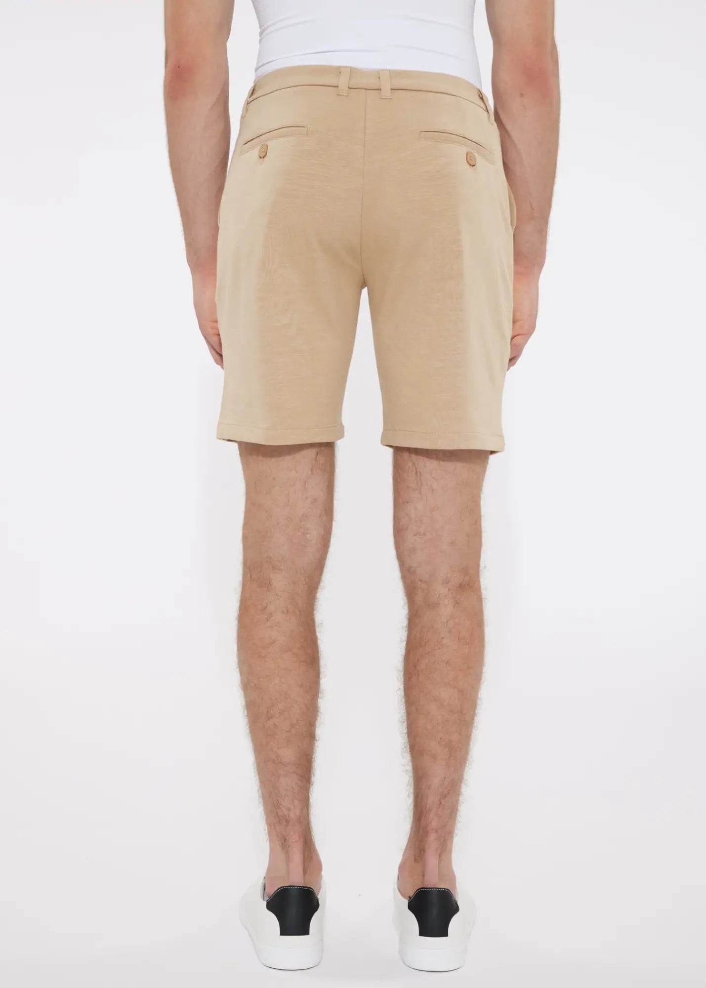 Beige solid stretch knit shorts with tailored fit and buttoned back pockets shown from the back side