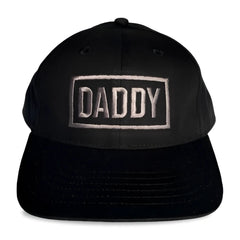 Black snapback cap with daddy embroidered in silver thread within a rectangular border by spunky monkee cap