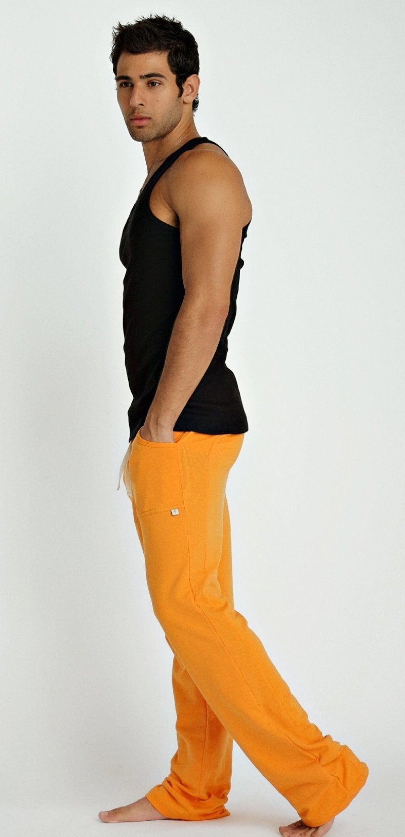 Bright orange loose-fitting pants with small white logo on thigh styled with black sustain tank top