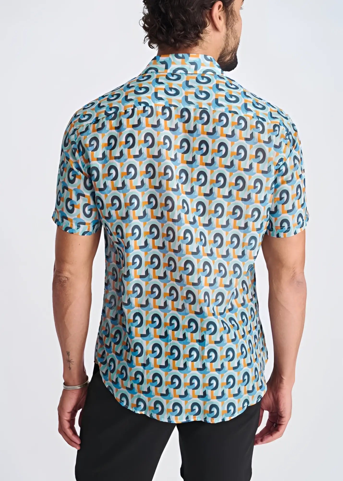 A man wearing a swirls lightweight cotton silk short-sleeved shirt with dark blue and orange geometric patterns on turquoise