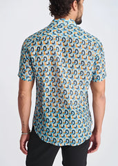 A man wearing a swirls lightweight cotton silk short-sleeved shirt with dark blue and orange geometric patterns on turquoise
