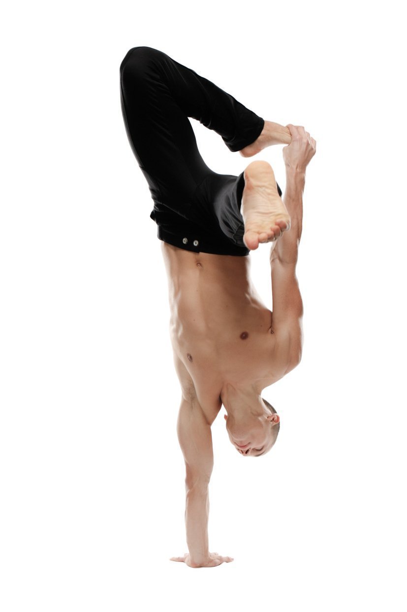 A muscular man performs an acrobatic handstand wearing black tactical urban at home dress pant yoga pant