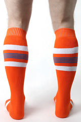 Bright orange tight end knee high athletic socks with white and navy blue horizontal stripes for sports use