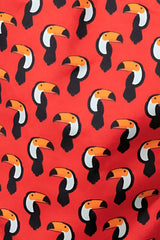 Red toucan print swim short fabric featuring a repeating pattern of stylized black white and orange toucans