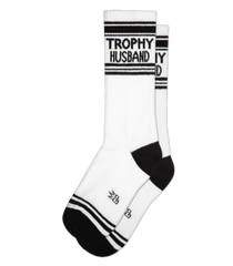 White athletic crew socks with black stripes and trophy husband text on cuff featuring a small logo near the toe