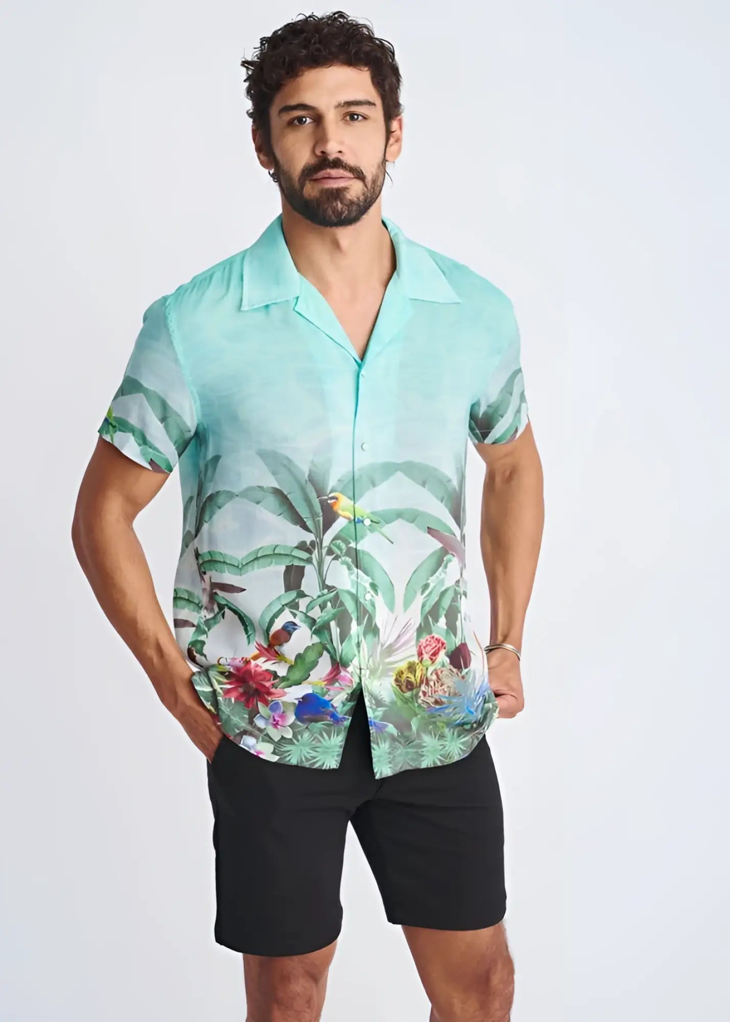 A men’s short-sleeved button-up modal shirt in vibrant turquoise with a tropical print of green leaves and colorful birds