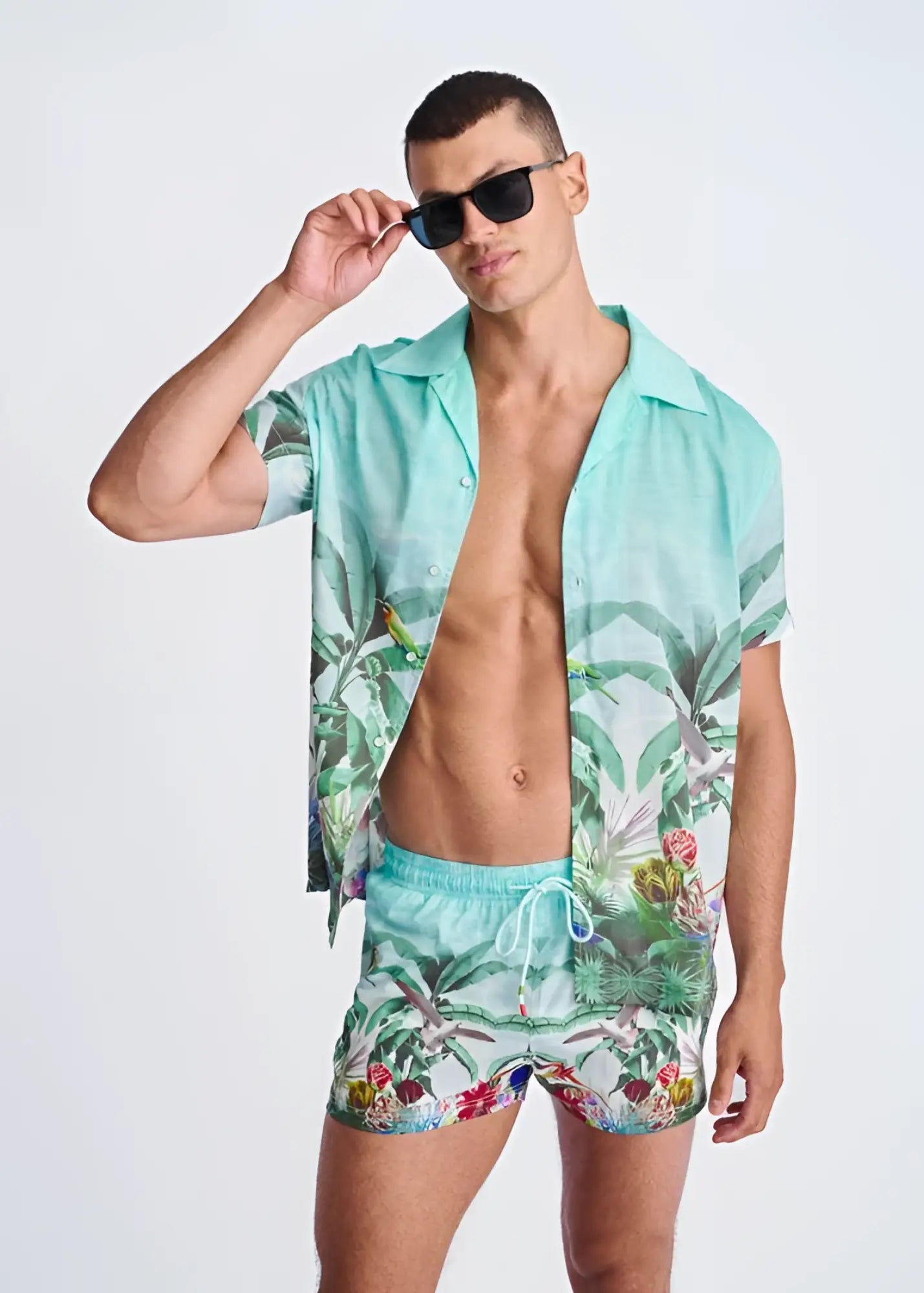 A vibrant turquoise tropical print swim shorts with mesh lining featuring palm leaves and birds pattern