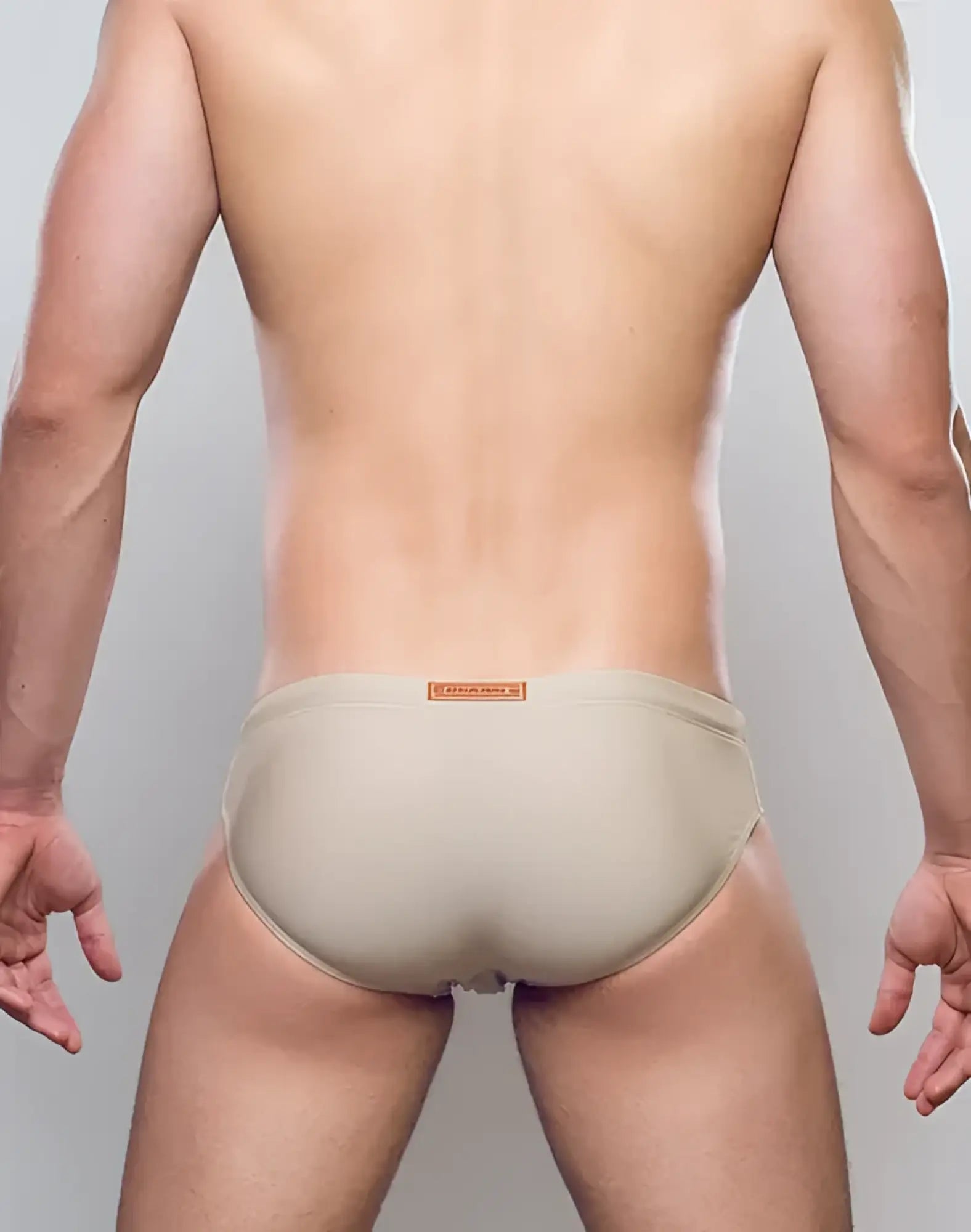 Beige form-fitting swim trunks with a subtle orange brand tag at the waistband from the v10 core bikini collection