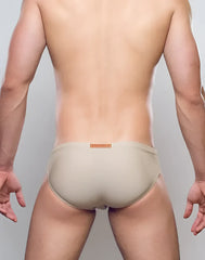 Beige form-fitting swim trunks with a subtle orange brand tag at the waistband from the v10 core bikini collection