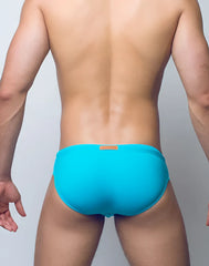 Bright turquoise v10 core bikini swim trunks with small orange brand tag at the waistband for swimming and beachwear
