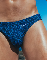 Dark blue swim brief with repeating light blue cursive script pattern and zeros brand name embroidered on waistband