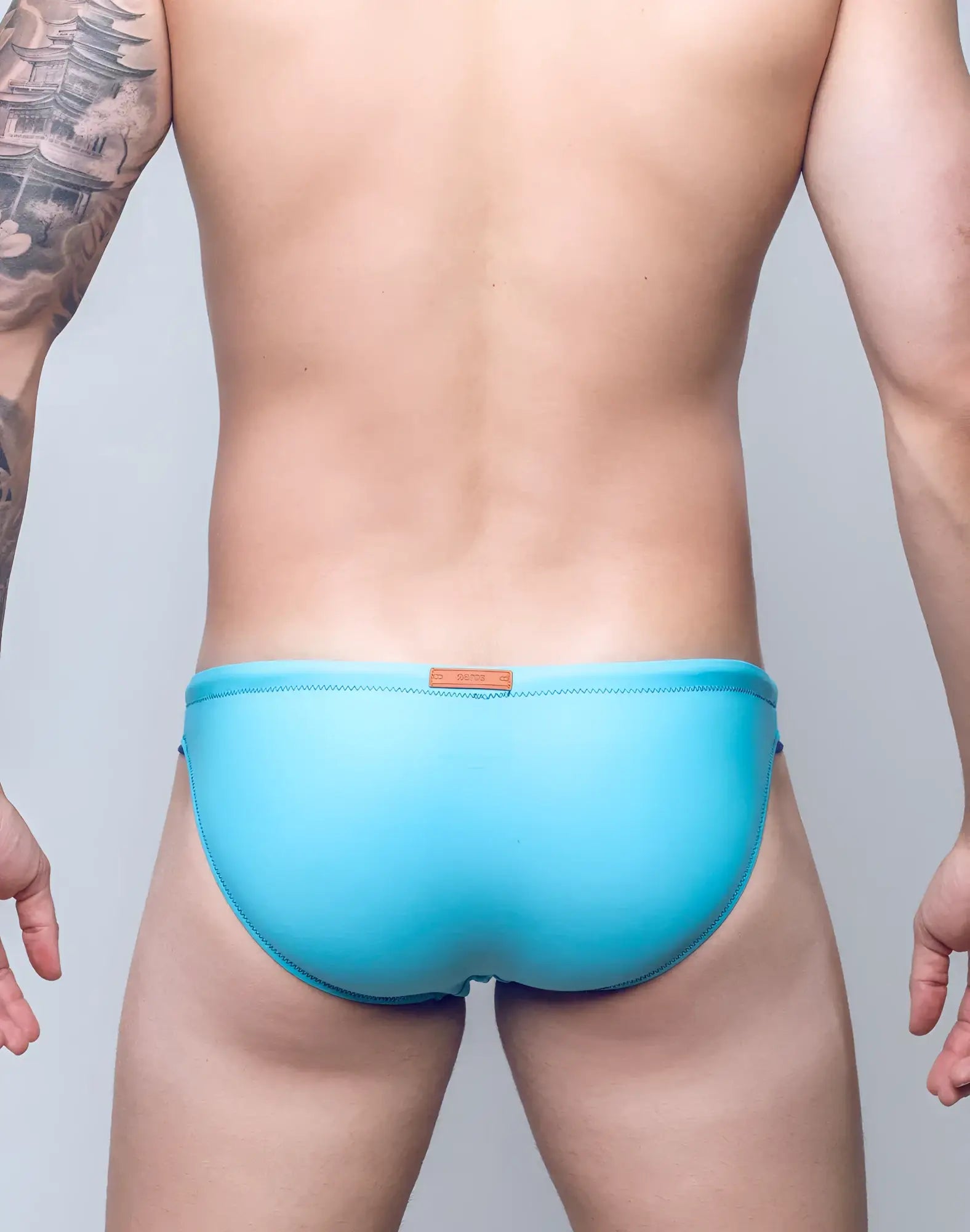 A sleek solid light blue v22 rapid swim brief with subtle stitched waistband and orange leather-like tag at the back side