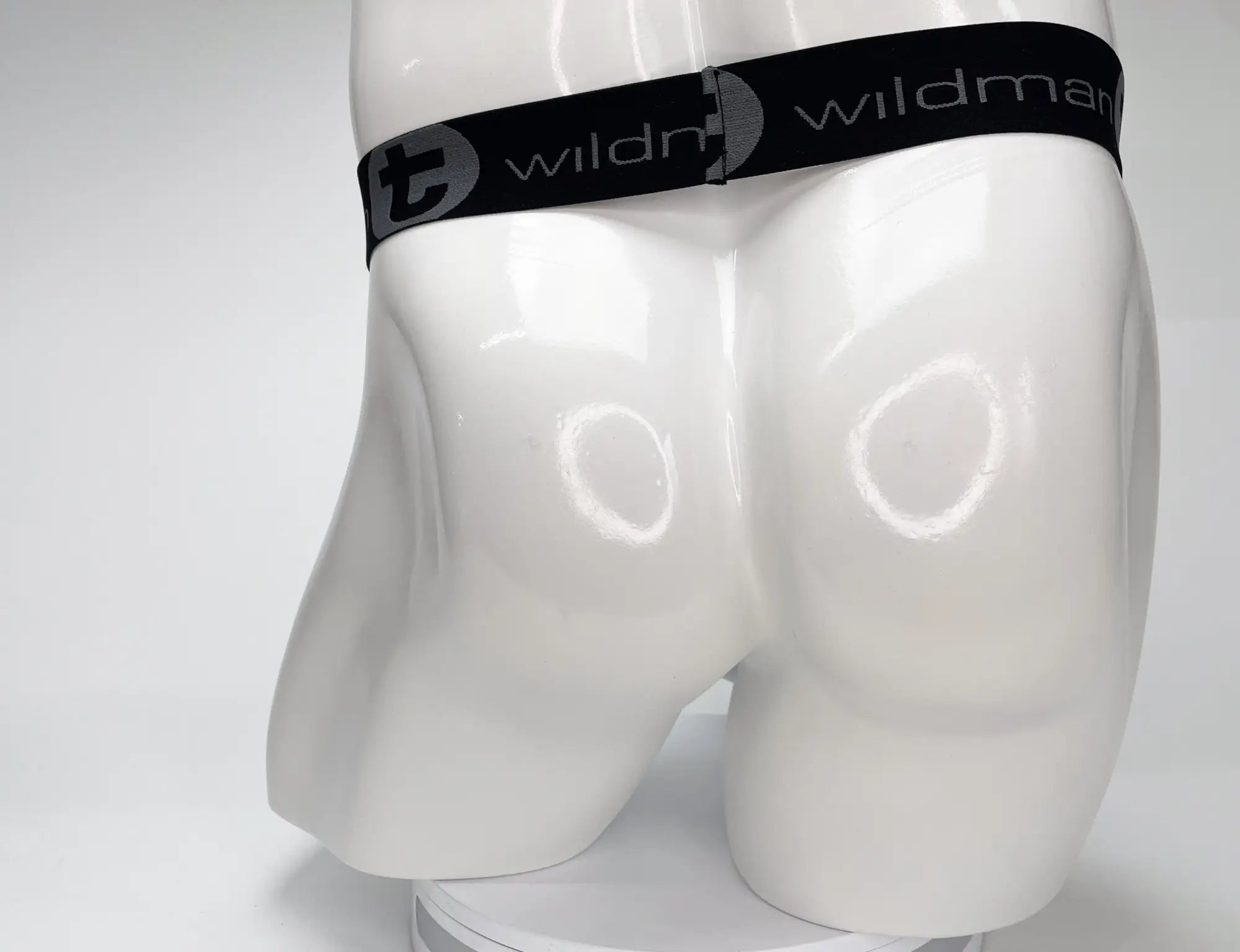 Black elastic waistband with wildman branding and stylized t logo on white mannequin for wildmant mesh monster cock strapless pouch white
