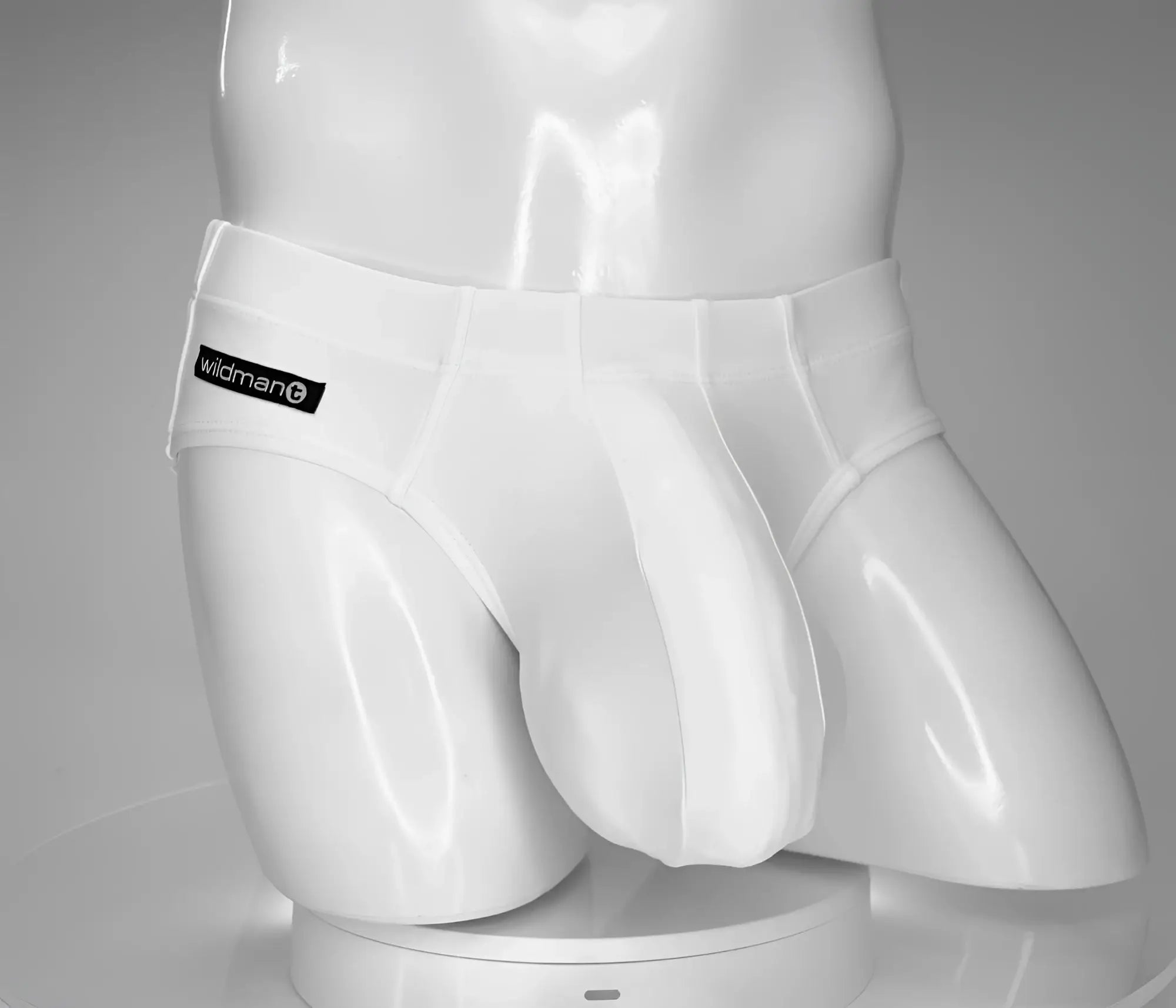 White glossy men’s swim briefs with black wildman brand label on waistband from wildmant monster cock collection