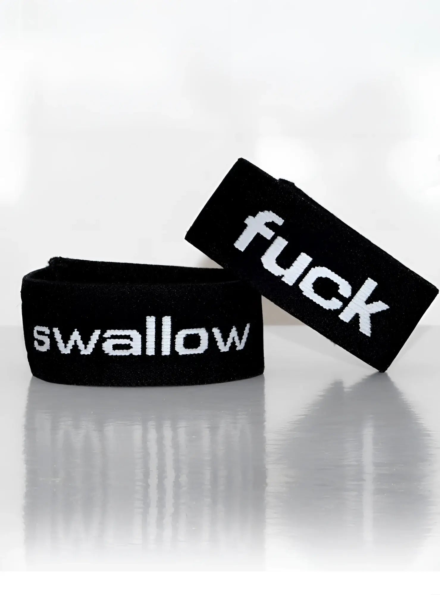 Black elastic wristband with white embroidered text reading fuck and swallow from wildmant verbal max cock-ring swallow