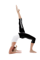 A woman in black 4/5 length zipper pocket capri yoga pants with silver stripes performs an upside-down handstand