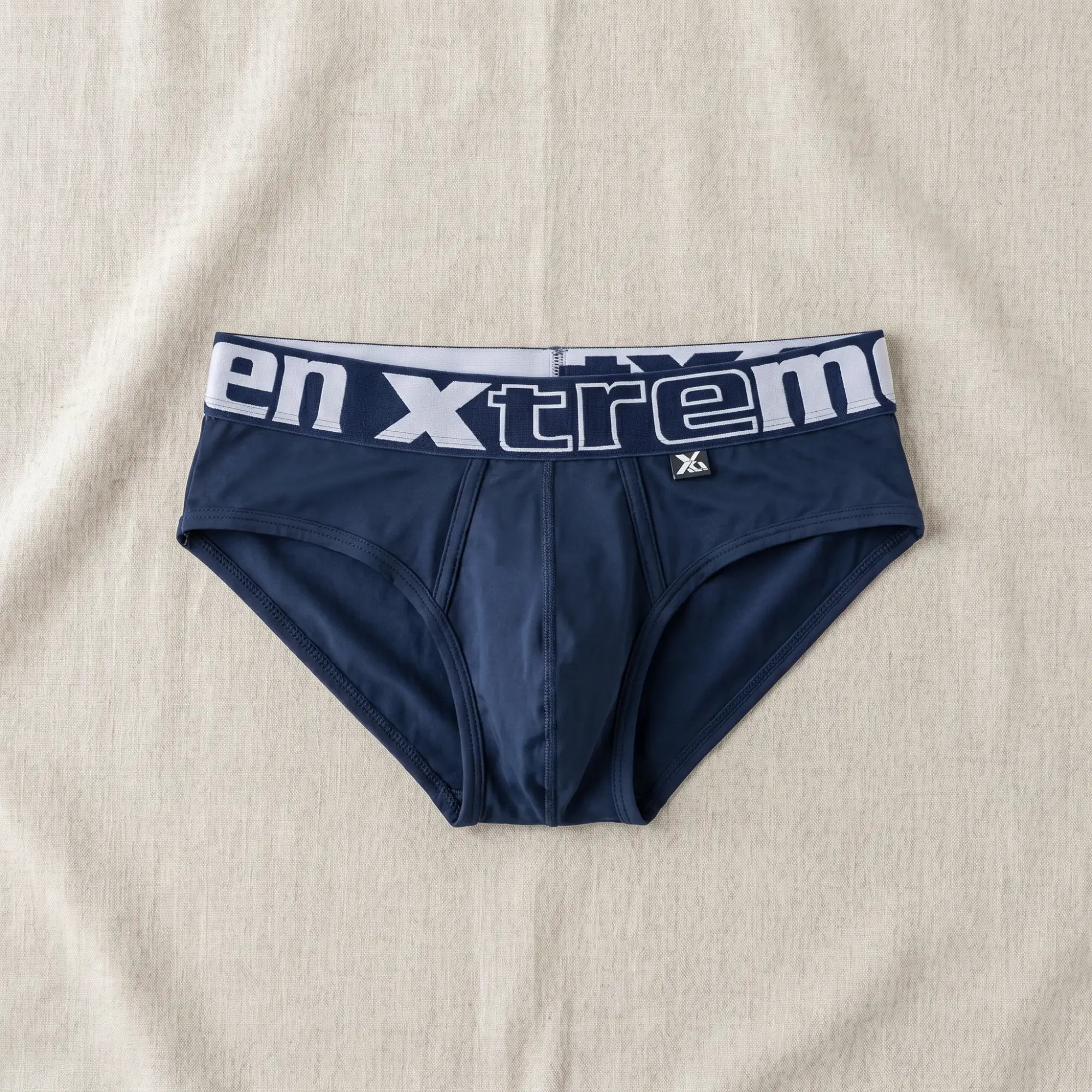 Navy blue mens microfiber briefs with white Xtremen waistband laid flat on neutral linen surface