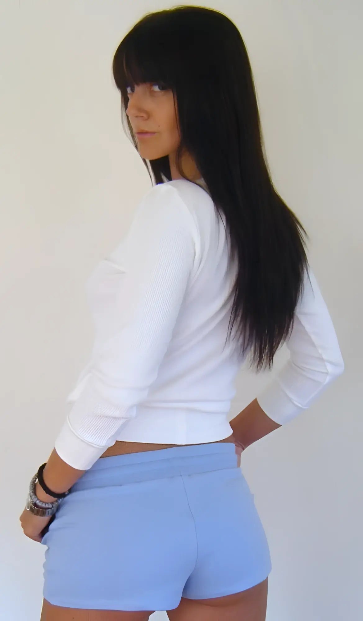 A woman wearing baby blue yoga training shorts and a white long-sleeved crop top in a fitness setting